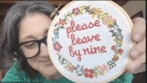 Photo of Robin DeRosa holding a knit sign that says "please leave by nine".