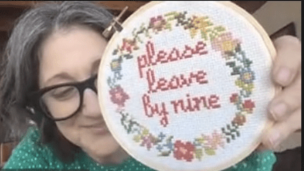 Photo of Robin DeRosa holding a knit sign that says "please leave by nine".