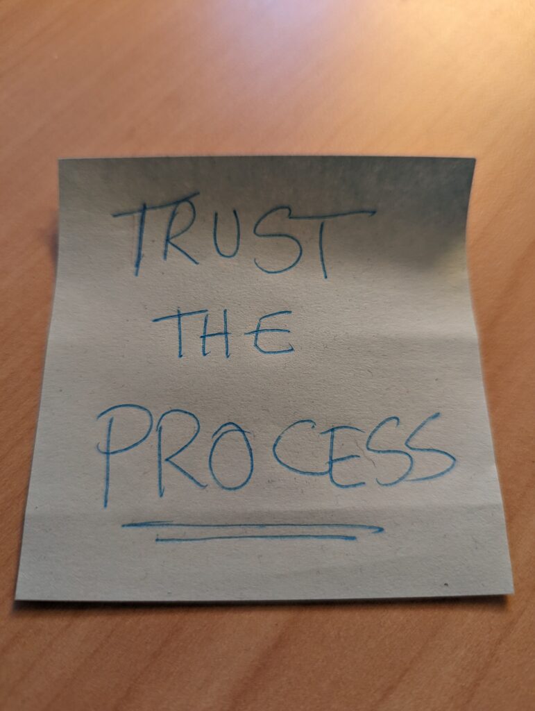 Photo of a sticky note that reads "Trust the process".